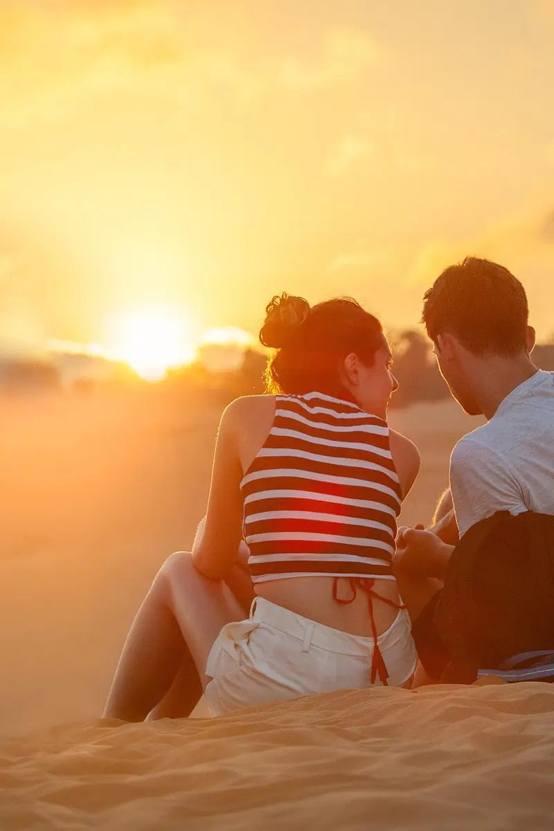 sundaycamper_contenbild_paar-sitzend Ein Paar sitzt auf einer Sanddüne im Sonnenuntergang